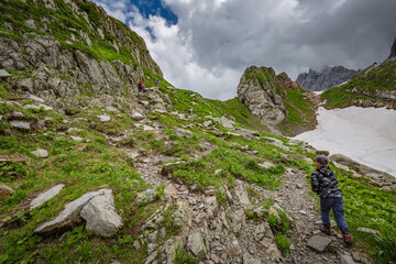 Mountain hiking Trail Road. Between Italy and Austria: near Volaia Lake Raunchkofer Mountain (Lago di Volaia Monte Rauchkofel). A little traveler climbs in the mountains with sticks.