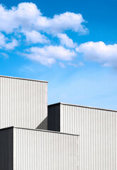 Fototapeta na wymiar Low angle view of 3 Corrugated Metal Industrial Buildings against clouds on blue sky background in vertical frame