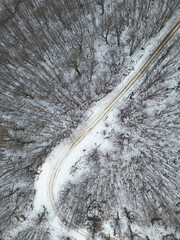 Wonderful snowy street with a sky with sun and clouds. The Gran Sasso d'Abruzzo in winter taken from above thanks to a drone. Woods and roads in winter to reach mountain paths.