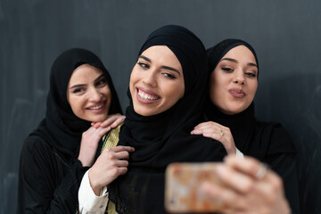 Group of young beautiful muslim women in fashionable dress with hijab using smartphone while taking...