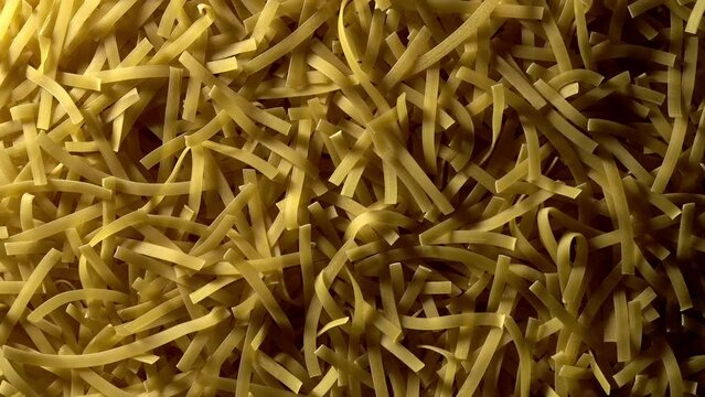 Uncooked Tagliatelle Lungo pasta rotating in slow motion - top view, flat lay, low key, food background. Raw dried organic golden long macaroni texture. Italian food, cuisine and culture close up