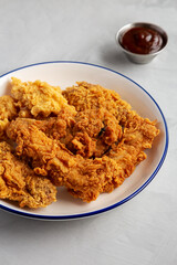 Chicken Popcorn, Wings and Tenders with BBQ Sauce on a plate on a gray background, side view.