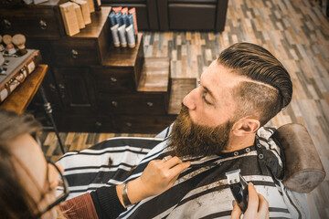 Hipster man at barbershop salon getting beard and hair cut - Hairdresser woman using hair clipper and comb for to modern gentleman cut - Barber shop concept