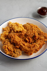 Chicken Popcorn, Wings and Tenders with BBQ Sauce on a plate on a gray background, side view.