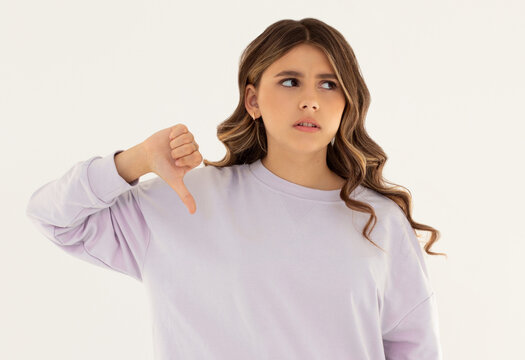 Young sad displeased unhappy woman wear purple sweater showing thumb down dislike gesture isolated on white background studio portrait. People lifestyle concept