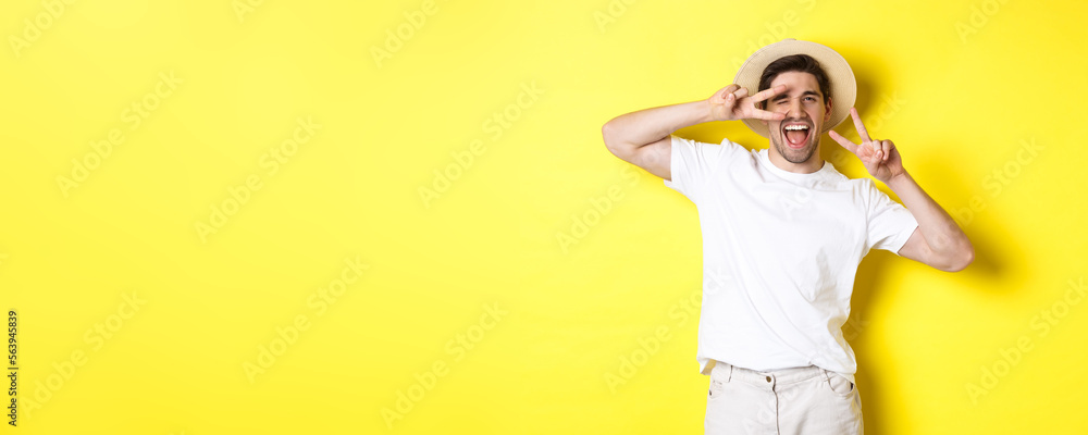 Wall mural Concept of tourism and vacation. Happy man tourist posing for photo with peace signs, smiling excited, standing against yellow background