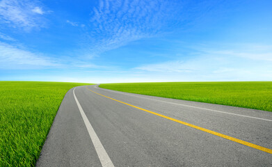 Tarmac road in grass field with blue sky background.