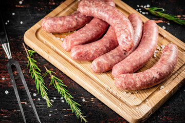 Raw sausages on a cutting board with a sprig of rosemary.