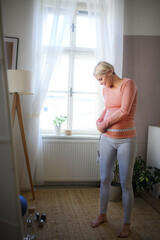Happy woman measuring her pregnant belly at home.
