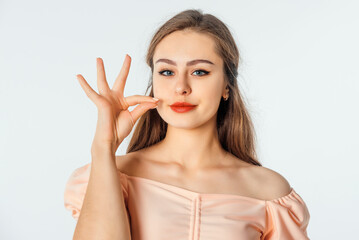 Fototapeta premium Portrait of young woman shows hush, shhh shush gesture, taboo, asks to keep quiet, gossiping, stands over white background
