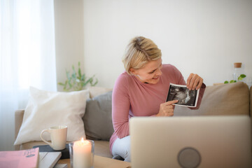 Pregnant woman showing ultrasound photo of her baby to webcam.