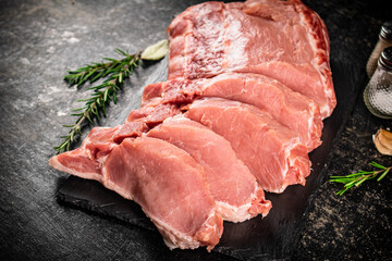 Pieces of raw pork on a stone board with rosemary and spices. 