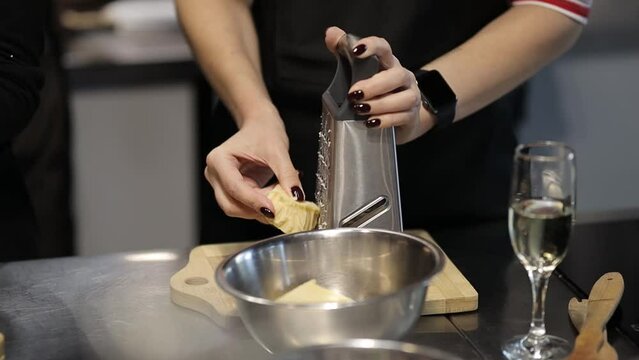 the cook rubs the cheese on a metal grater, close-up. The girl rubs the cheese with a metal grater, close-up. Slow motion. a chef in a black apron grates cheese, at a culinary master class, close-up