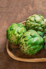 Fototapeta premium Artichoke flower buds. Fresh and raw artichoke on the wooden table. Copyspace. Top view.