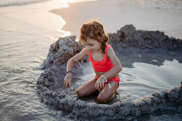 Little girl playing on the beach, digging hole in sand.