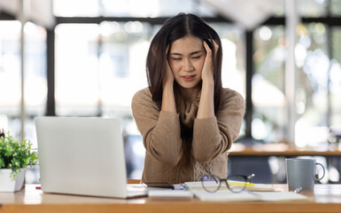 Obraz premium Tired Young freelance asian business woman with headache at office, feeling sick at work, Sad, unhappy, Worried, Depression, or employee life stress concept.