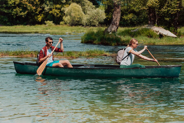 Couple adventurous explorer friends are canoeing in a wild river surrounded by the beautiful nature