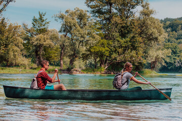 Couple adventurous explorer friends are canoeing in a wild river surrounded by the beautiful nature