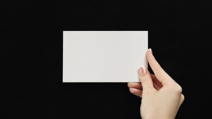 Mockup note. Empty letter. Text presentation. Female hand holding white clean blank paper sheet with copy space on black advertising background.