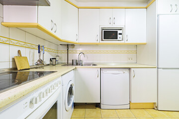 L-shaped kitchen furnished with white cabinets, pale yellow countertops and white built-in...