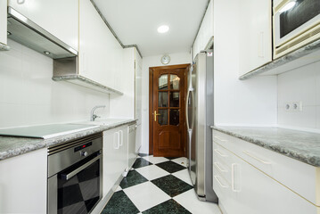 Apartment with a kitchen furnished on both walls with white cabinets with white metal handles and gray granite countertops and checkered stoneware floors