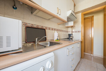 Small elongated kitchen with white furniture and built-in appliances of the same color and details...