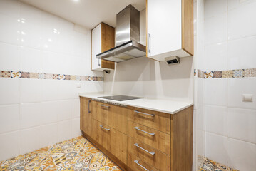 Kitchen with chestnut wood cabinets with light-coloured countertops, white tiles with a border and hydraulic stoneware floors