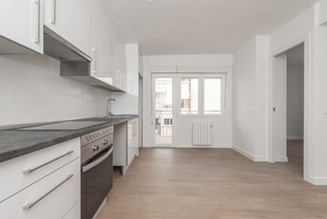 Newly installed kitchen furniture with white wall and base units, gray countertop in an open room with access to a terrace