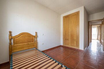 Bedroom with a built-in wardrobe with oak doors, red stoneware floors and a bed with a wooden box...