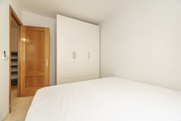 Bedroom with a double bed and a white three-section wardrobe and an oak door