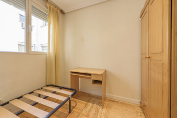 Bedroom with oak wardrobe, cheap desk, box spring without mattress and wooden flooring