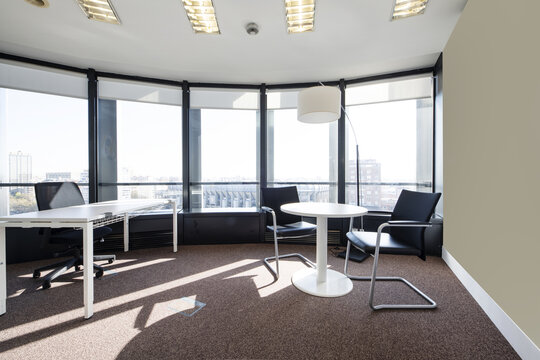 Office with a small white round table next to a large window with views, a rectangular table, carpeted floors, curved walls and a technical ceiling