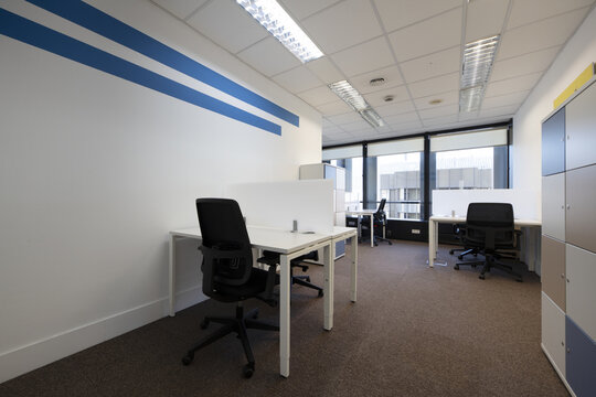 Office with small opposite white tables with partitions, filing cabinet with locks and black swivel chairs