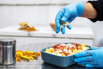 Gloved hands of a chef preparing a bowl of bacon chips with cheese gratin