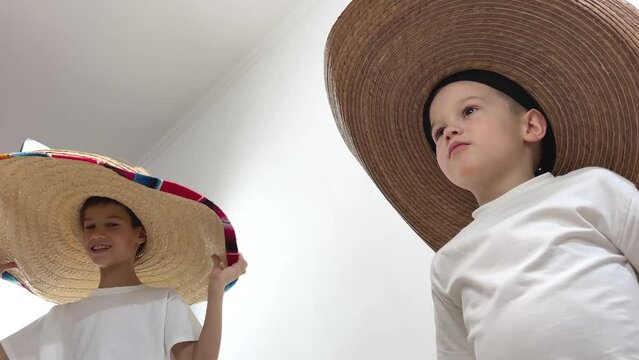 shooting from below two boys on white background in huge hats Mexican with a red rim of multi-colored stripes and a cowboy boy playing trying on hats White t-shirts of different ages