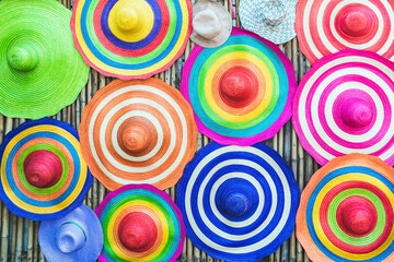 A variety of fashionable and colorful hats hanging on the bamboo backdrop of curbside shop. Women's...