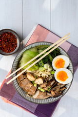 Asian noodle soup, ramen with chicken breast, vegetables, mushrooms and egg on a checkered napkin on a white wooden table in sunlight. Top view, healthy eating concept.