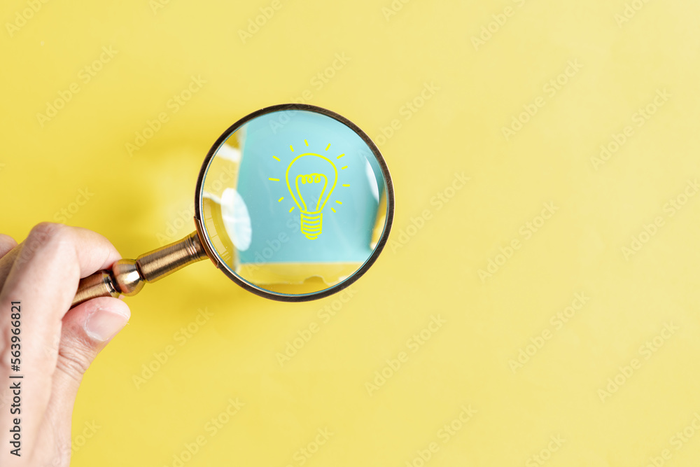 Aufkleber light bulb hiding of yellow punched paper, hand holding magnifier focus to lightbulb icon target for