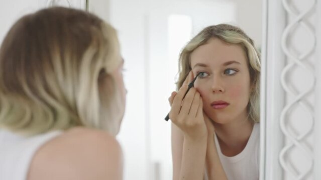 Teenage girl doing makeup with black eyeliner.