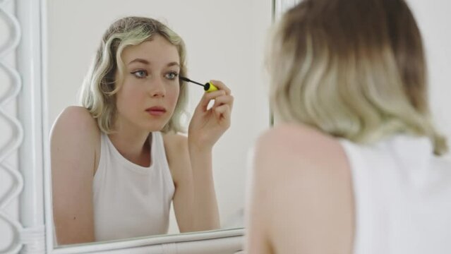 Teenage girl applying black mascara on lashes.