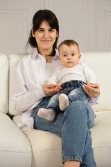 Fototapeta premium Portrait of a young loving mother with a small child in his arms sitting on the sofa