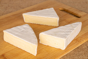 Three slices of delicious brie cheese with wooden kitchen board on jute cloth, macro.