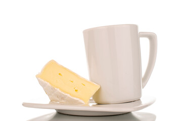 One piece of fragrant Brie cheese on a white ceramic saucer with a white cup, macro, isolated on white background.