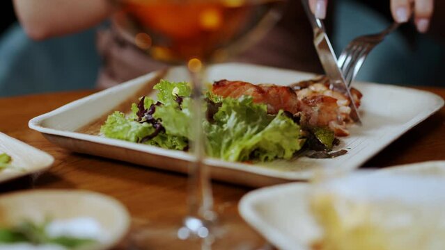 A girl cuts a steak on a plate with a fork and a knife, close-up. Dinner in a restaurant