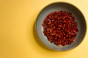 Fresh Pomegranate in a Blue Bowl on Pastel Yellow Background.