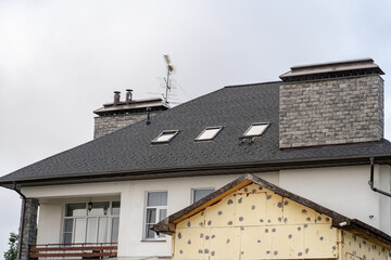 Suburban stucco house with TV antenna, balcony and drainage system on metal roof. Roof gutter...