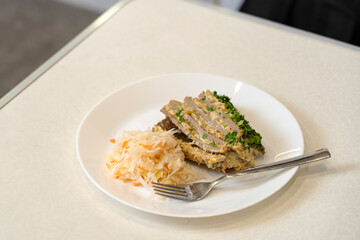 A piece of liver pie lies on white plate of sauerkraut, on table. 