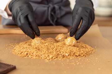 Woman in black gloves holds candy. Soft focus. Professional pastry chef or chocolatier. Sweets in waffle crumbs