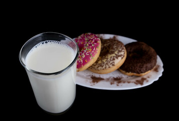 Tasty colorful doughnuts with glass of milk isolated on black background