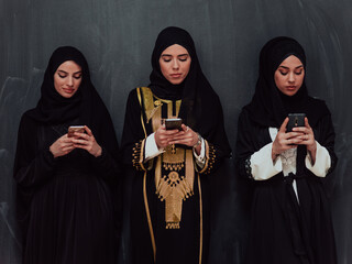 group of beautiful muslim women in fashionable dress with hijab using mobile phone in front of...